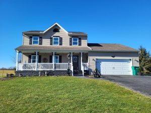 20240203_110451-1 home after a remodeling project with tan siding, large front porch, and black window shutters