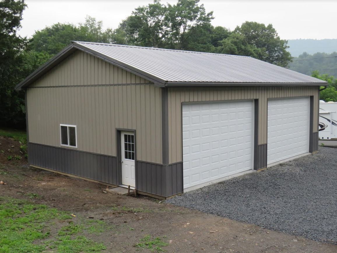 garage with tan siding, one entry door, two garage doors, and gray metal roof