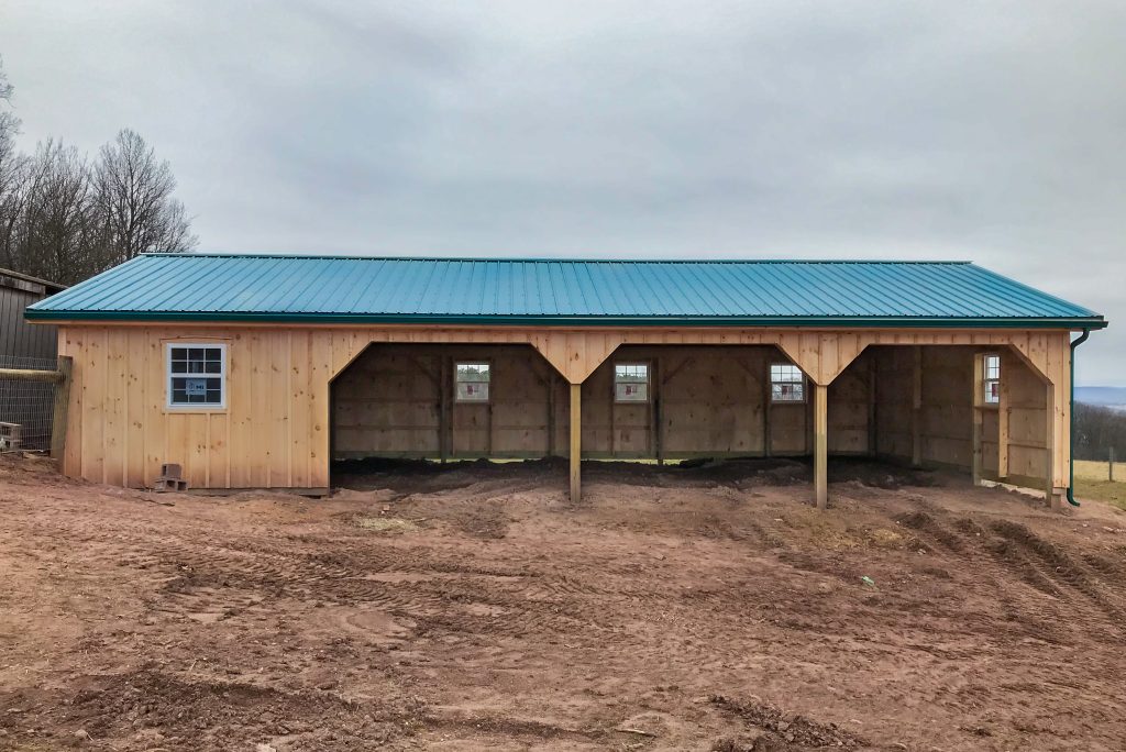 open pole barn with wooden siding and green roof 