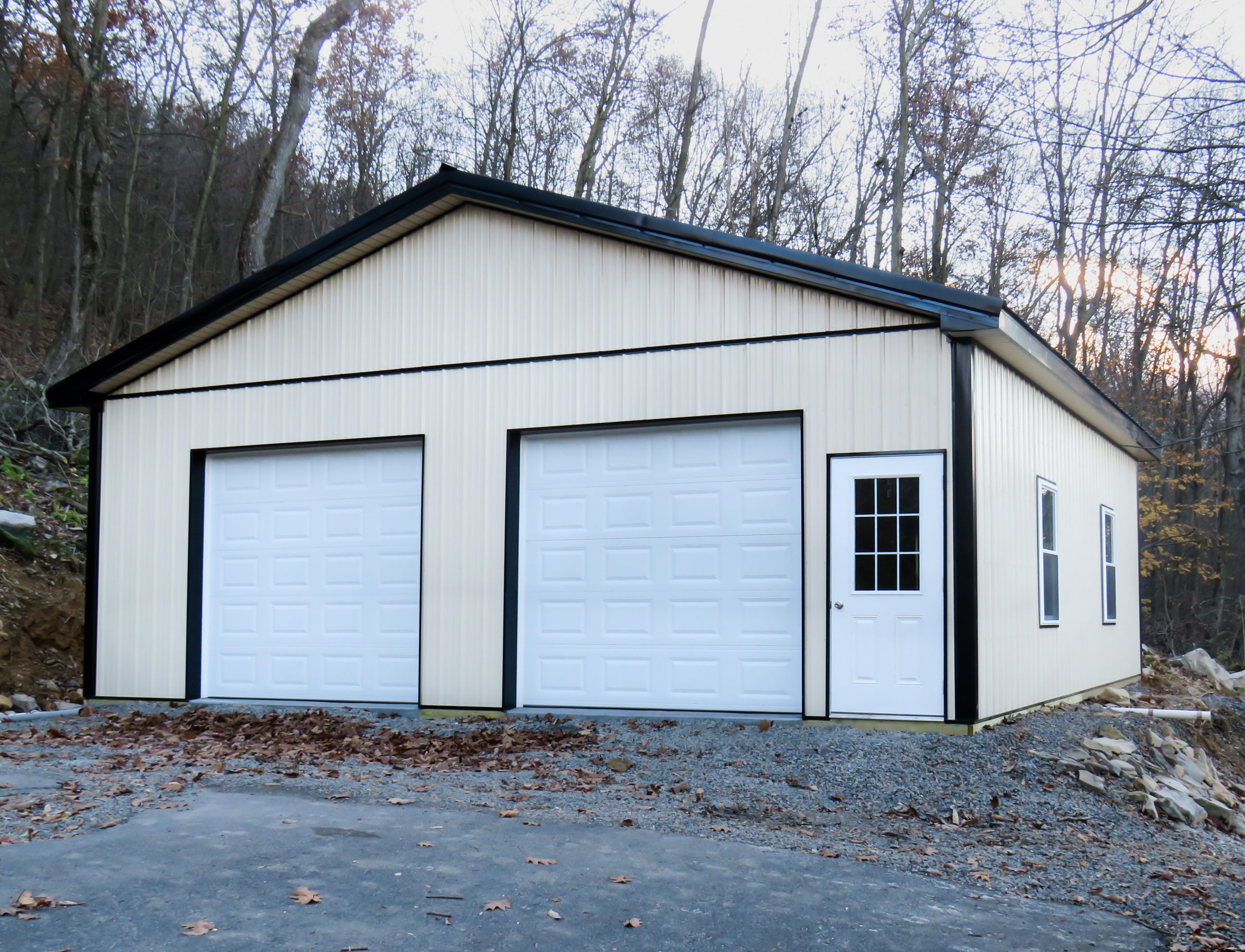 pole barn with white metal siding, black trim, one entry door, and two garage doors